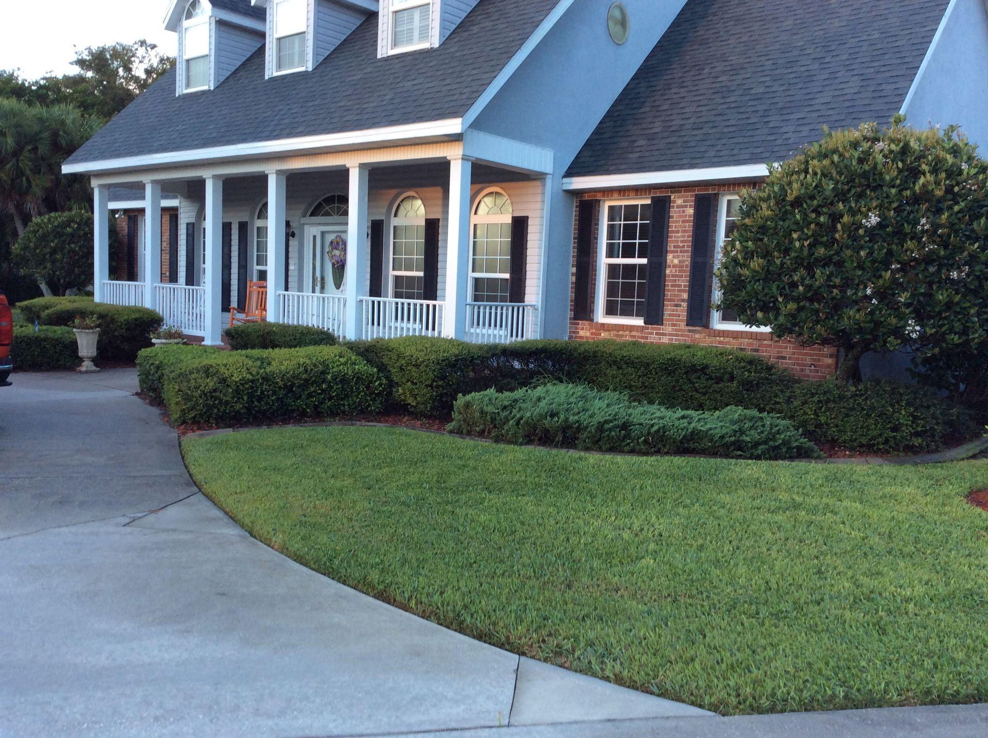 Front view of a large house with a porch, manicured lawn, and surrounding bushes.