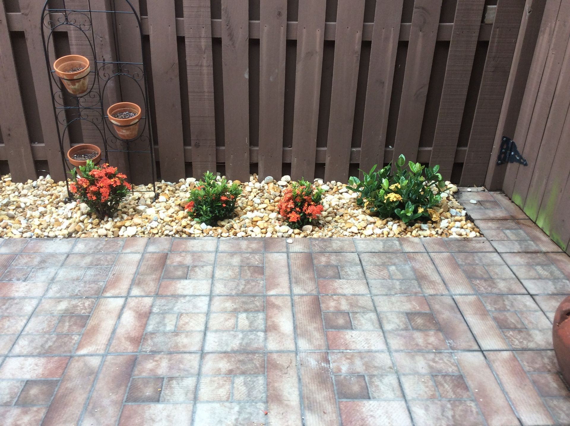 Outdoor garden area with potted plants and flowers, surrounded by gravel, near a wooden fence.