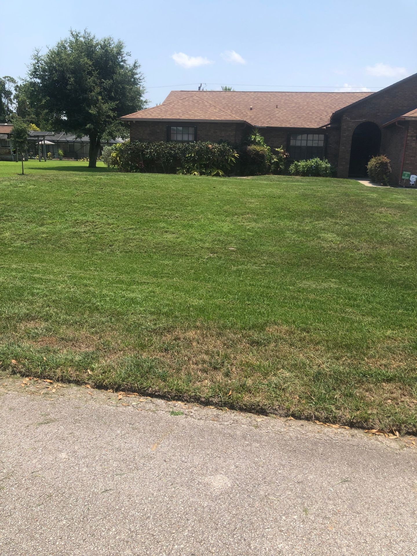 Residential brick house with a neatly mowed front lawn and trees under a clear blue sky.